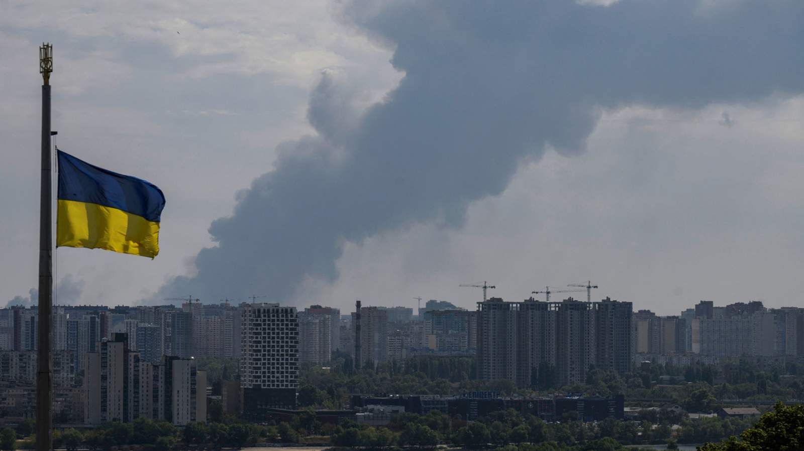 Украинский флаг развевается на фоне дыма, поднимающегося после воздушной атаки в Киевской области. Украина. 27 августа 2026 года. Фото: Vladyslav Musiienko / AFP / Scanpix / LETA